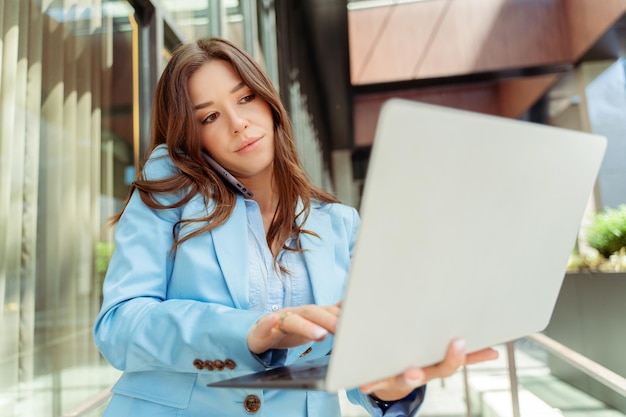 Foto donna d'affari attraente che indossa una giacca blu che usa un portatile e parla al cellulare multitasking