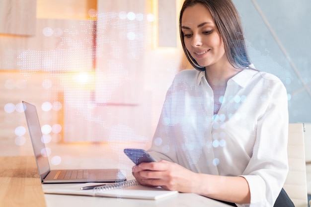 Attractive businesswoman in white shirt using smart phone to check new candidates for international business consulting HR social media icons over modern office background