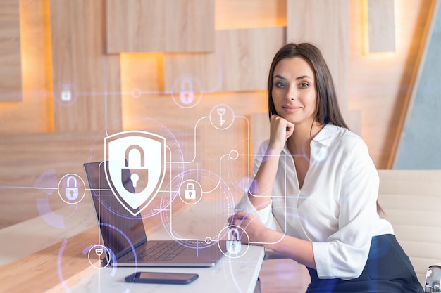 Attractive businesswoman in white shirt at workplace working with laptop to defend customer cyber security Concept of clients information protection Padlock hologram over office background