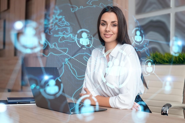 Attractive businesswoman in white shirt at workplace working with laptop to hire new employees for international business consulting HR social media hologram icons over office background