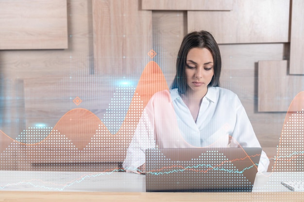 Attractive businesswoman in white shirt at workplace working\
with laptop to optimize trading strategy at corporate finance fund\
forex chart hologram over office background