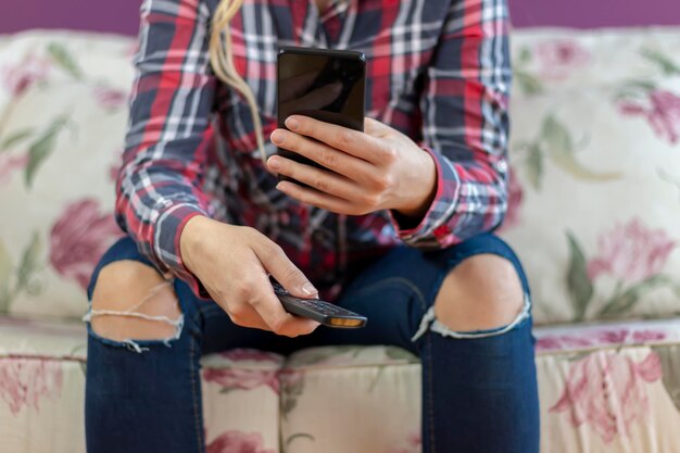 Photo attractive casual woman using smart phone and holding remote control in her hand