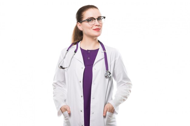 Attractive caucasian brunette female doctor standing in office smiling with hands in pockets