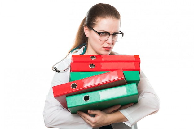 Attractive caucasian brunette sad female doctor standing in office with binders in her hands on white 