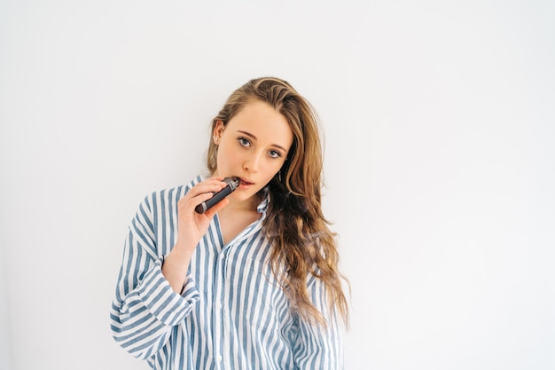 Photo attractive caucasian female against white wall she is using a electronic cigar