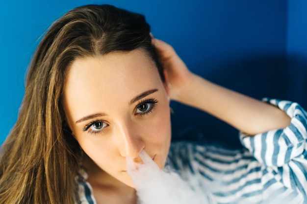 attractive caucasian female against white wall She is using a electronic cigar