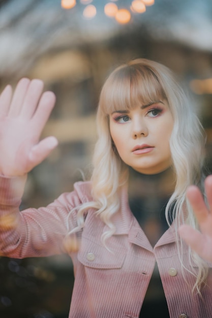 Attractive Caucasian female wearing a black turtleneck shirt and a pink jacket posing behind glass