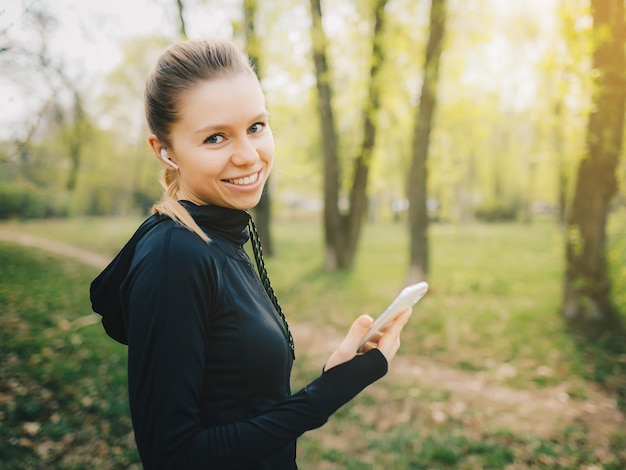 スポーツスーツのワイヤレスヘッドフォンで黄色の孤立した背景に魅力的な白人の女の子は、トレーニングを実行し、水を飲む