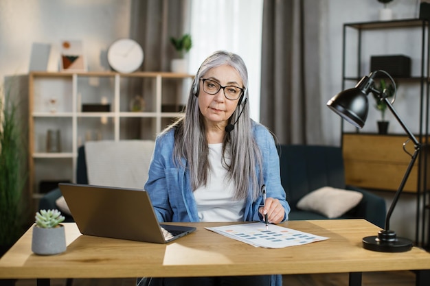 Attractive caucasian greyhaired woman sitting at desk and typing on laptop