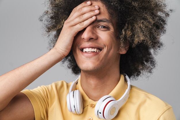 attractive caucasian man with afro hairstyle wearing headphones laughing isolated over gray wall