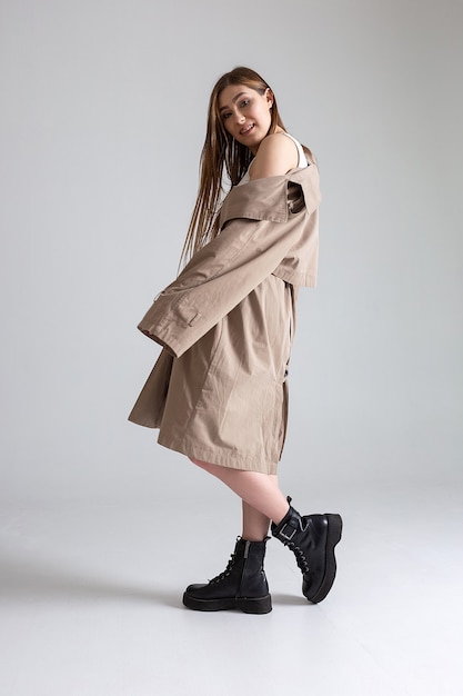 Attractive caucasian skinny girl in raincoat posing on white studio cyclorama