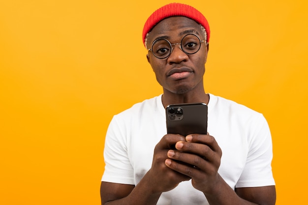 Attractive charming black man in a white T-shirt with a smartphone in his hands on a yellow studio with copy space