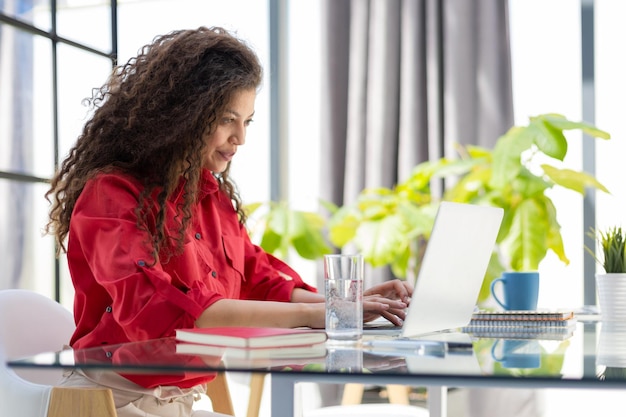 Attractive cheerful business woman in red shirt working on laptop at modern office