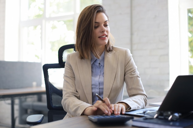 Attraente donna d'affari allegra che lavora al computer portatile in un ufficio moderno.