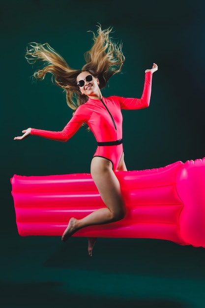 Attractive cheerful woman in a pink swimsuit on an isolated background she has an inflatable mattress between her legs Vacation concept Slender girl in sunglasses on an air mattress