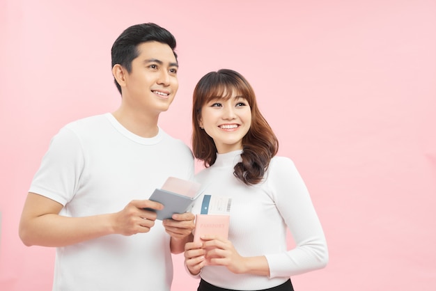 attractive cheerful young couple  standing isolated over pink background, showing passport with flight tickets