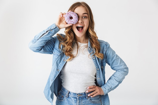 Attractive cheerful young girl standing isolated over white , holding tasty donut