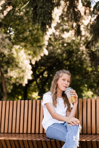 Attractive child girl drinking summer lemonade Summer cocktails Happy girl holding cup with orange lemonade outdoor