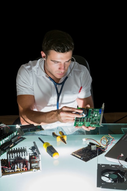 Attractive computer engineer examining hardware with stethoscope by night