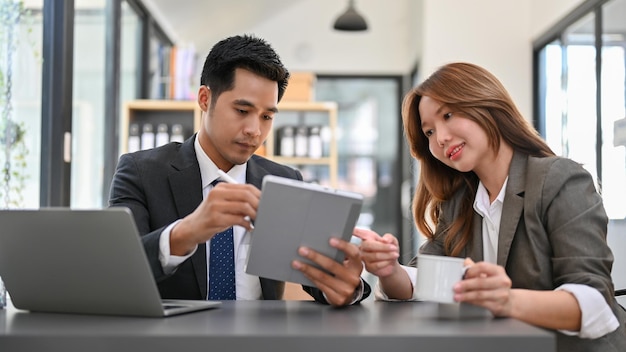 Attractive and confident Asian businesswoman having coffee while talking with a male colleague