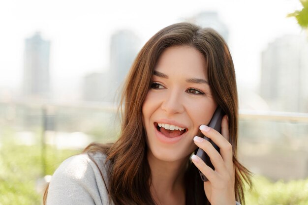 魅力的な自信のある女性が携帯電話で話し,外でコピースペースを眺めています.