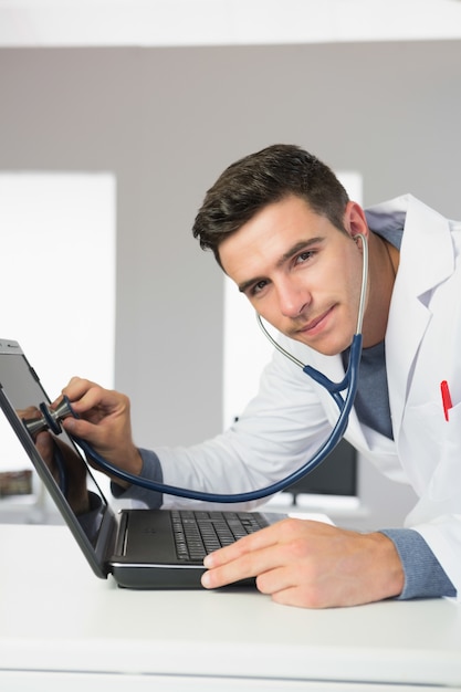 Attractive content computer engineer examining laptop with stethoscope