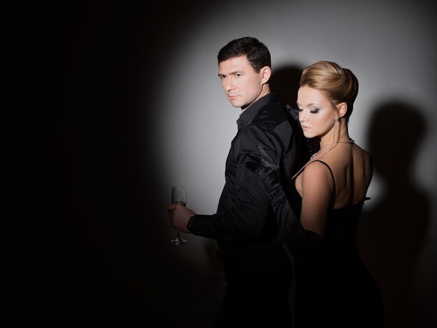 An attractive couple in black stylish and elegant young man and woman in the spotlight beautiful blo...