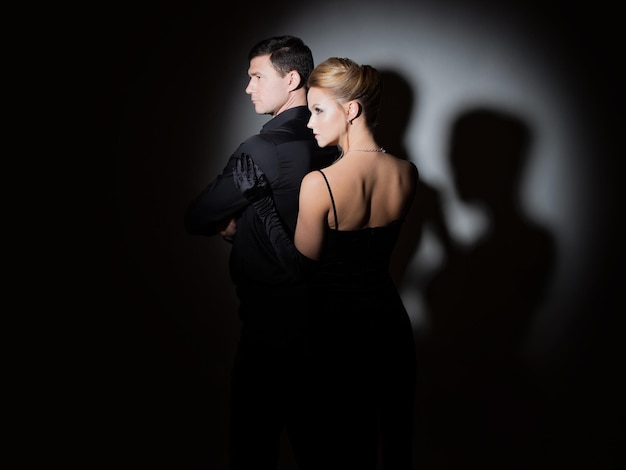 An attractive couple in black stylish and elegant young man and woman in the spotlight beautiful blo...