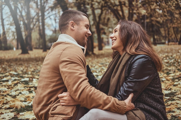 Photo attractive couple have fun while sitting at autumn park full of golden leaves.