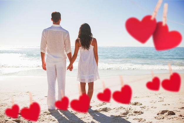 Attractive couple holding hands and watching the waves against hearts hanging on a line