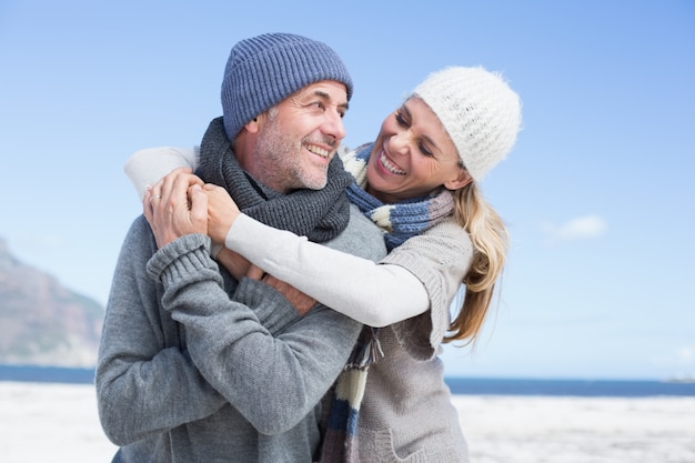 Attractive couple hugging on the beach in warm clothing