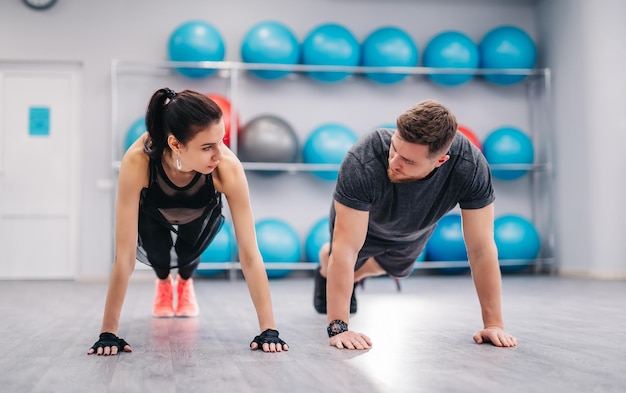 Attractive couple pushing off the floor and looking at each other in the gym Active man and woman in sportswear exercising together