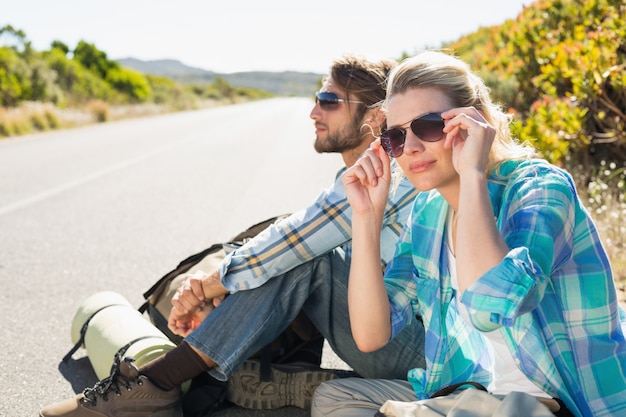 Photo attractive couple sitting on the road hitch hiking