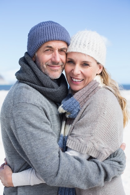 Attractive couple smiling at camera on the beach in warm clothing