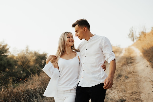 Attractive couple in white clothes looking at each other, smiling and walking on nature.