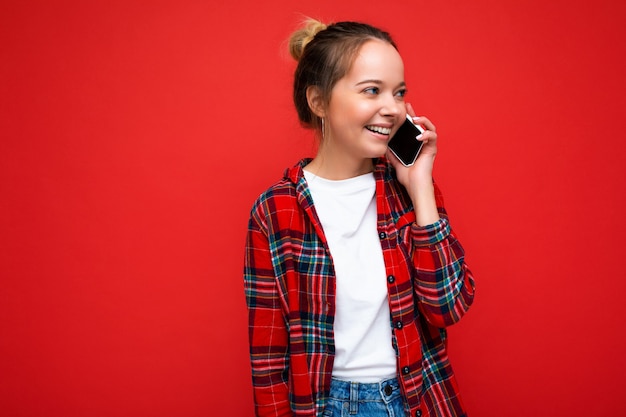 赤の上に孤立して立っている魅力的なかわいい肯定的な笑顔の若いブロンドの女性