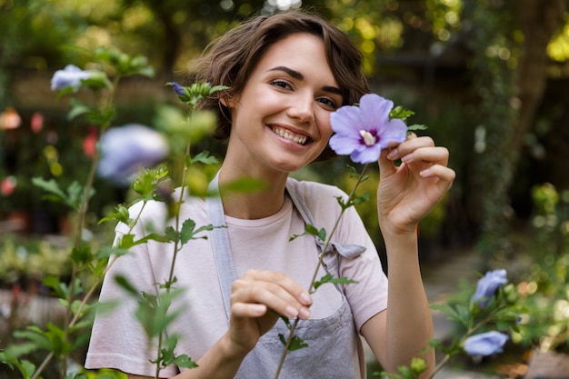 温室の花の植物の上に立っている魅力的なかわいい女性の庭師