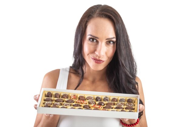チョコレートでいっぱいのキャンディーボックスを喜んで保持している魅力的な黒髪の女性孤立した背景