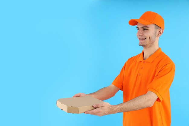 Attractive delivery man with pizza box on blue background