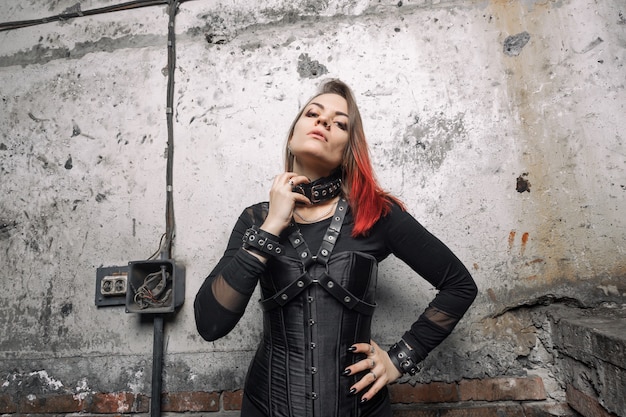 attractive dominant woman with piercings and bright hair in a black corset, with leather harnesses and bracelets posing