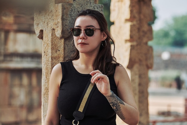 Attractive east asian woman in black sunglasses and black clothes stands among ancient pillars