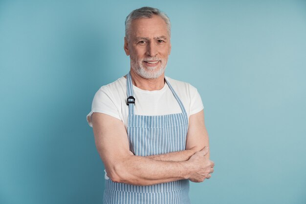 Attractive, elderly man in a blue apron posing on a blue wall