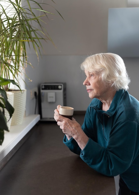 an attractive elderly woman drinks espresso in the kitchen and looks out the window