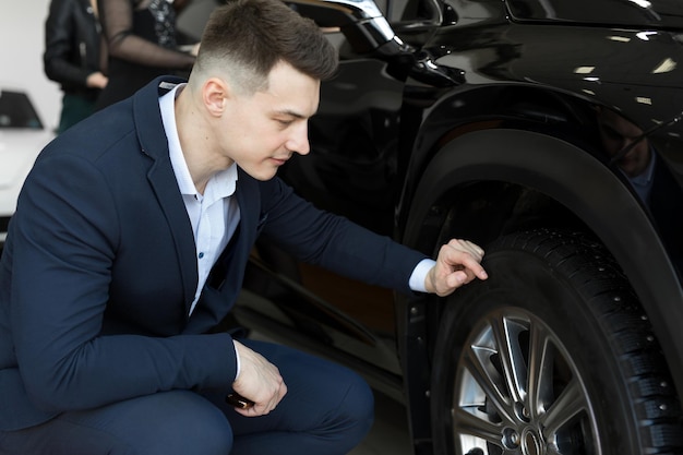 Attractive elegant man examining wheels of a new automobile on sale at dealership