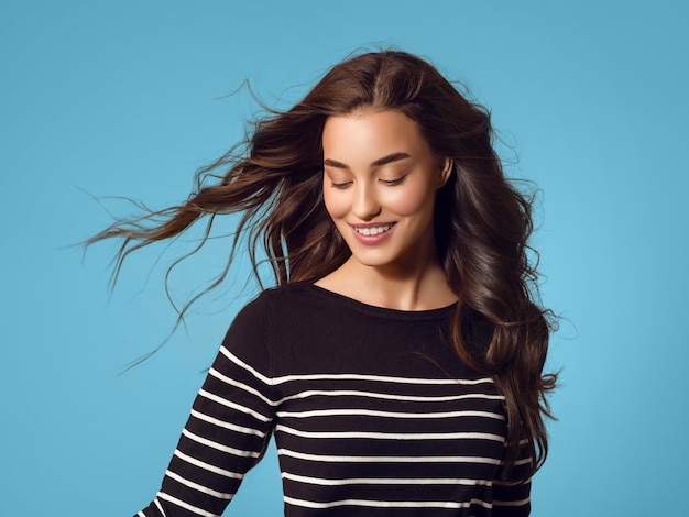 Attractive emotional happy woman with beautiful fly hair in stripes hands up dancing studio portrait