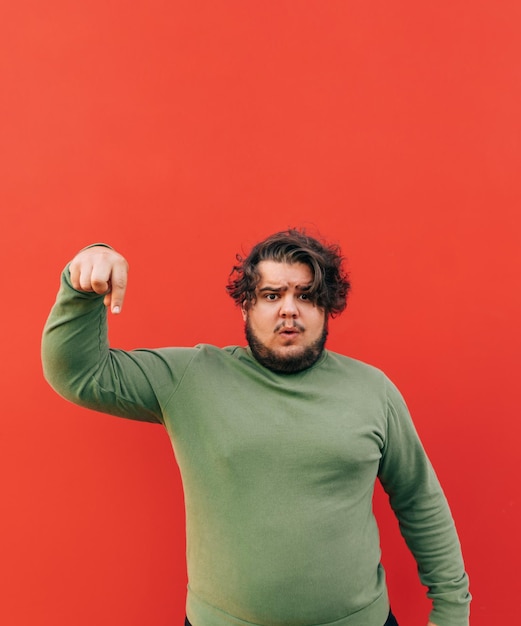 привлекательный эмоциональный латиноамериканец, стоящий на красном фоне, указывая пальцем вниз