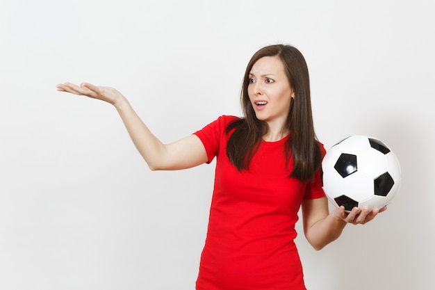 Привлекательная европейская молодая грустная расстроенная женщина, футбольный фанат или игрок в красной форме держит футбольный мяч, беспокоится о потере команды, изолированной на белом фоне. Спорт, игра в футбол, концепция образа жизни.
