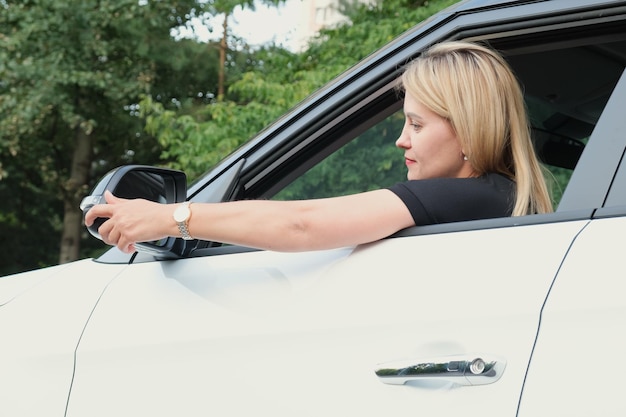 Attractive fairhaired woman driving a car straightens the car side mirror with her hand