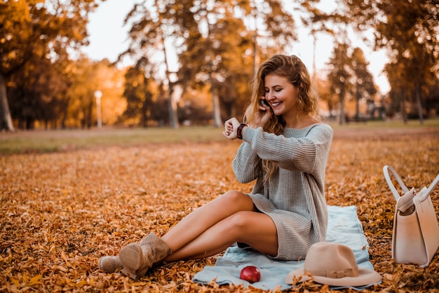 Attractive fashion blogger talking on phone in autumn park.