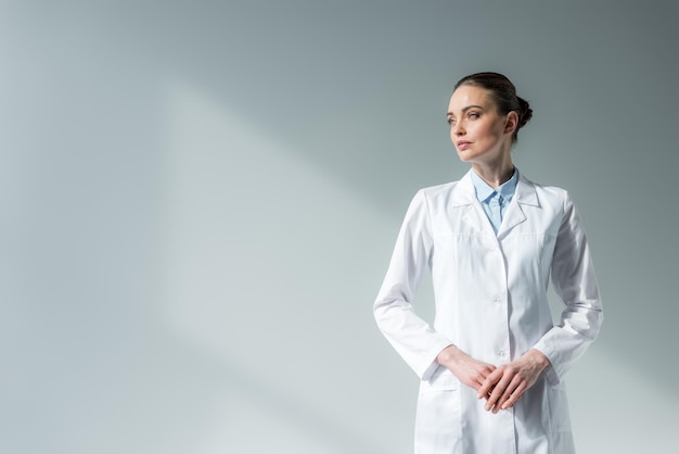 Foto attraente dottoressa in camice bianco che distoglie lo sguardo sul grigio